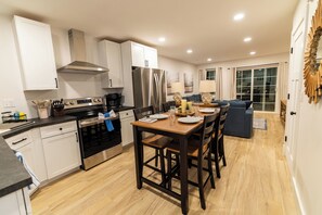 A modern kitchen with a dining area, wooden flooring, and a view of the outdoors through a sliding glass door.