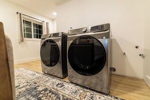 Two front-loading washing machines in a room with a patterned rug, a window with curtains, and a door with a handle.