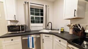 A modern kitchen with white cabinetry, a stainless steel dishwasher, a microwave, a sink with a faucet, and a stove.