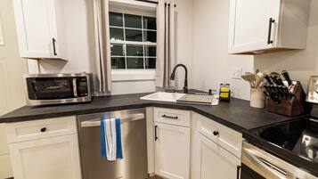 A modern kitchen with white cabinetry, a stainless steel dishwasher, a microwave, a sink with a faucet, and a stove.