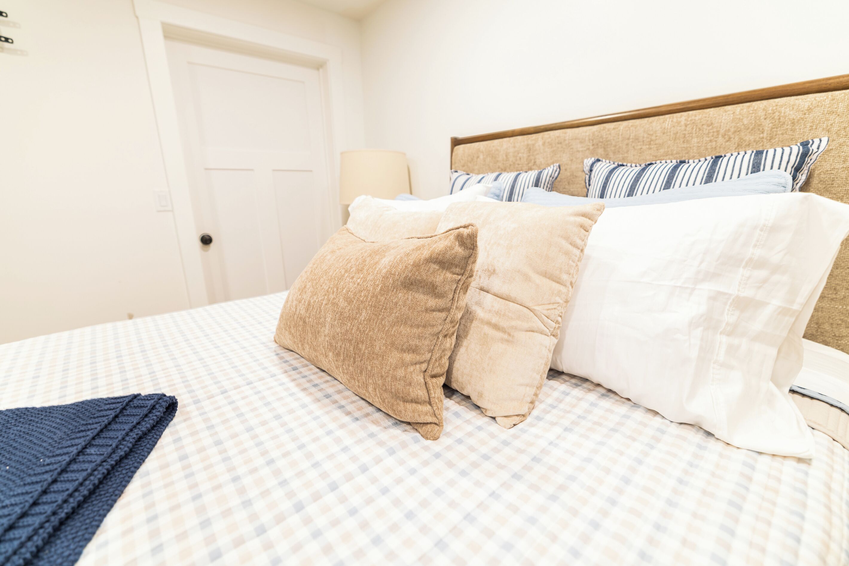 Een net opgemaakt bed met een geruit sprei, meerdere kussens en een blauwe gebreide deken.