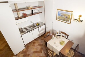 A compact kitchen with a stove, sink, and shelves, a dining table with chairs, and a painting on the wall. - Casa Tera A: A graceful two-story apartment in the characteristic style of the Tuscan countryside, with Free WI-FI. (Grosseto)