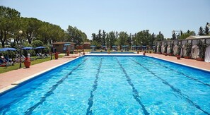 A rectangular swimming pool with clear blue water, surrounded by lounge chairs and umbrellas, with trees and a building in the background. - Casa Tera A: A graceful two-story apartment in the characteristic style of the Tuscan countryside, with Free WI-FI. (Grosseto)