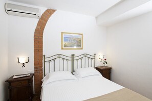 A bedroom with a brick arch, a bed with white linens, a nightstand with a lamp, and a wall-mounted air conditioner. - Casa Tera A: A graceful two-story apartment in the characteristic style of the Tuscan countryside, with Free WI-FI. (Grosseto)