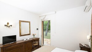 Un dormitorio con cama, televisor sobre una cómoda de madera, espejo y puerta que da a un área exterior.