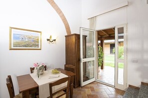 Ein Essbereich mit Tisch für zwei Personen, einer Holzkommode, einem Gemälde an der Wand und einer Schiebeglastür, die zu einem Außenbereich führt.