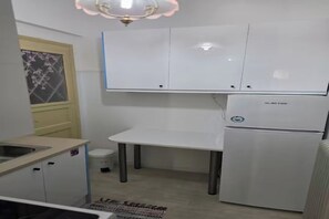 Pieni, käytännöllinen keittiö, jossa on valkoiset kaapit, jääkaappi ja pesuallas.