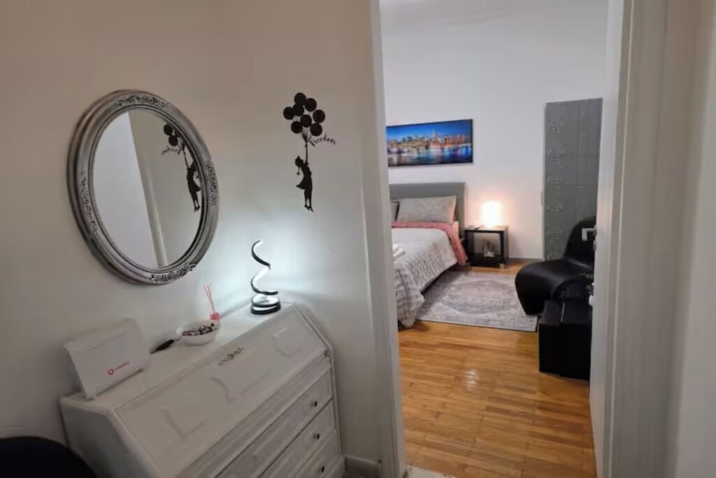 A bedroom with a bed, bedside table, lamp, and a wall with a cityscape painting.