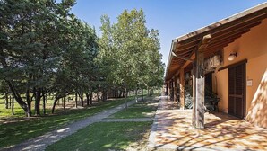 A pathway leading to a building with a covered porch and a grassy area with trees. - Casa Tera B: A graceful two-story apartment in the characteristic style of the Tuscan countryside, with Free WI-FI. (Grosseto)