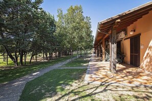 A pathway leading to a building with a covered porch and a grassy area with trees. - Casa Tera B: A graceful two-story apartment in the characteristic style of the Tuscan countryside, with Free WI-FI. (Grosseto)