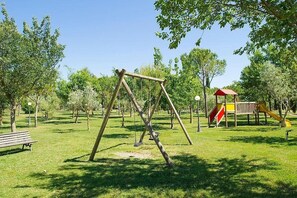 Ein Park mit einer Holzschaukel, einer Bank und einem Spielplatz mit einer Rutsche.