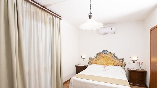 Una habitación de hotel con cama, mesitas de noche, lámpara, equipo de aire acondicionado y cortina.