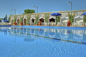 Ein Schwimmbecken mit Liegestühlen und Sonnenschirmen, umgeben von einer überdachten Terrassenanlage.