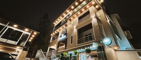 A two-story building with a balcony, a staircase, and a car parked in front.