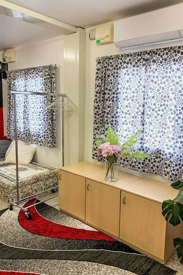 A room with a bed, a bedside table with a vase of flowers, a floor lamp, and a window with a patterned curtain.