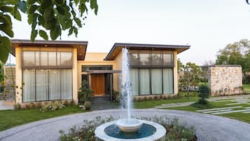 A modern two-story house with a central water feature and a stone wall.