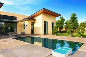 Una casa moderna con piscina, mobiliario de exterior y un jardín bien cuidado.
