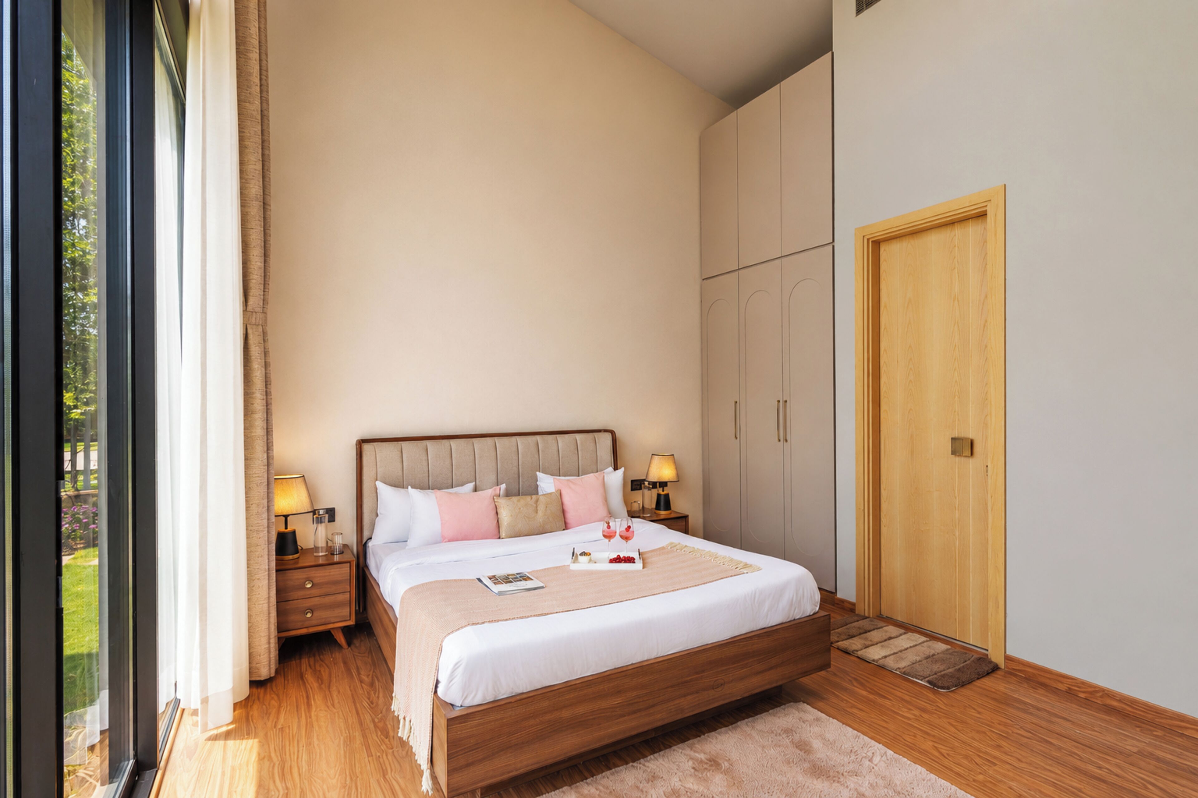 A bedroom with a wooden bed, bedside tables, a wardrobe, and a large window.
