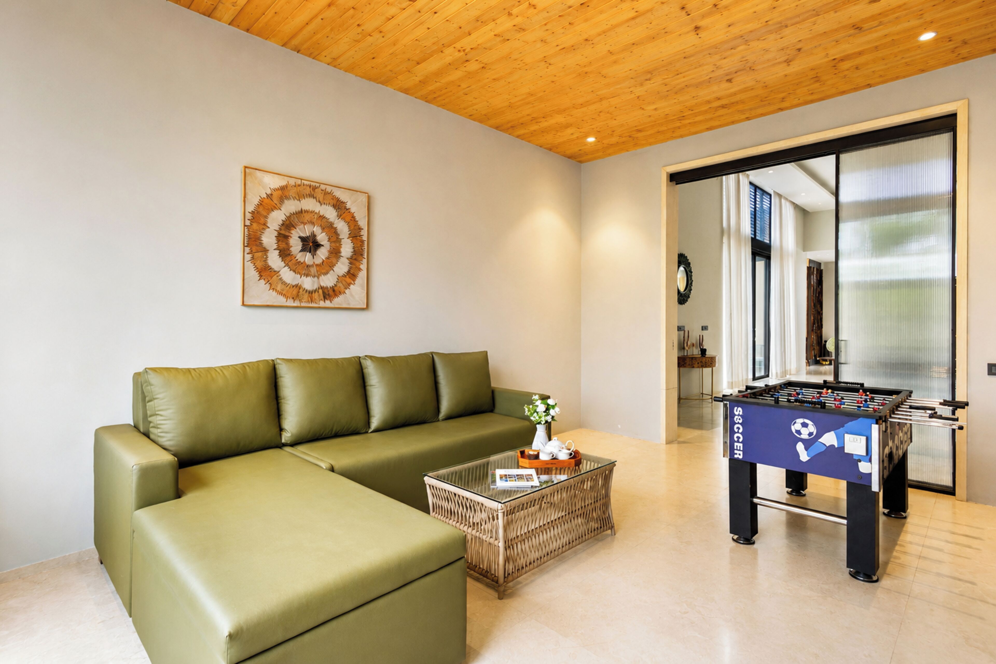 A modern living room with a green sofa, a glass coffee table, and a foosball table.