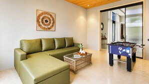 Una sala de estar moderna con un sofá verde, una mesa de centro de vidrio y una mesa de futbolín.