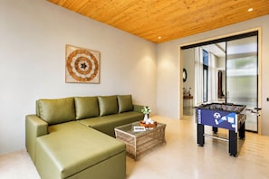 Una sala de estar moderna con un sofá verde, una mesa de centro de vidrio y una mesa de futbolín.