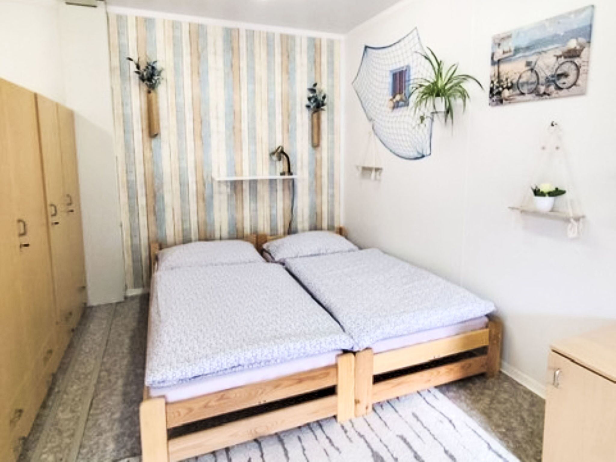Une petite chambre avec un lit simple, un mur à rayures, une armoire en bois, une petite étagère avec une plante et un tableau encadré accroché au mur.
