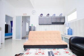 A room with a bed, a sofa, a water dispenser, a clock, and a cabinet with decorative plates. - Cozzy Villa Biru (Jawa Timur)