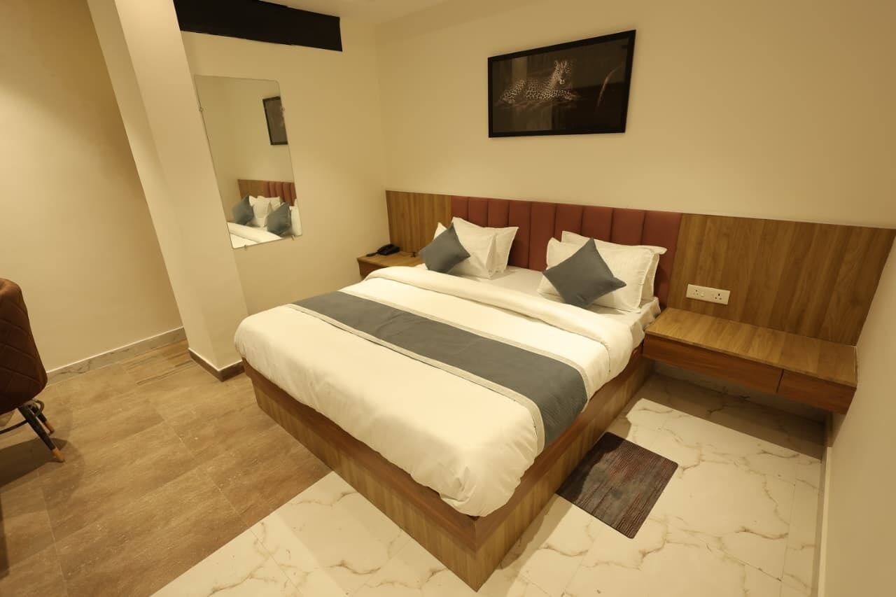 A hotel room with a bed, a nightstand, a mirror, and a wall-mounted artwork.