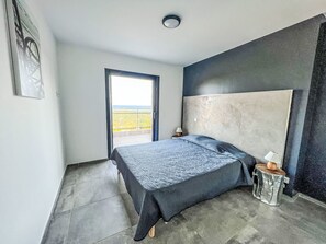 Ein Schlafzimmer mit Bett, Nachttisch, Lampe, Fenster und Tür.