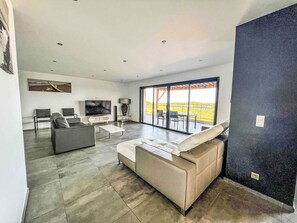 Ein modernes Wohnzimmer mit einer Couch, einem Fernseher und einem Essbereich mit Stühlen.