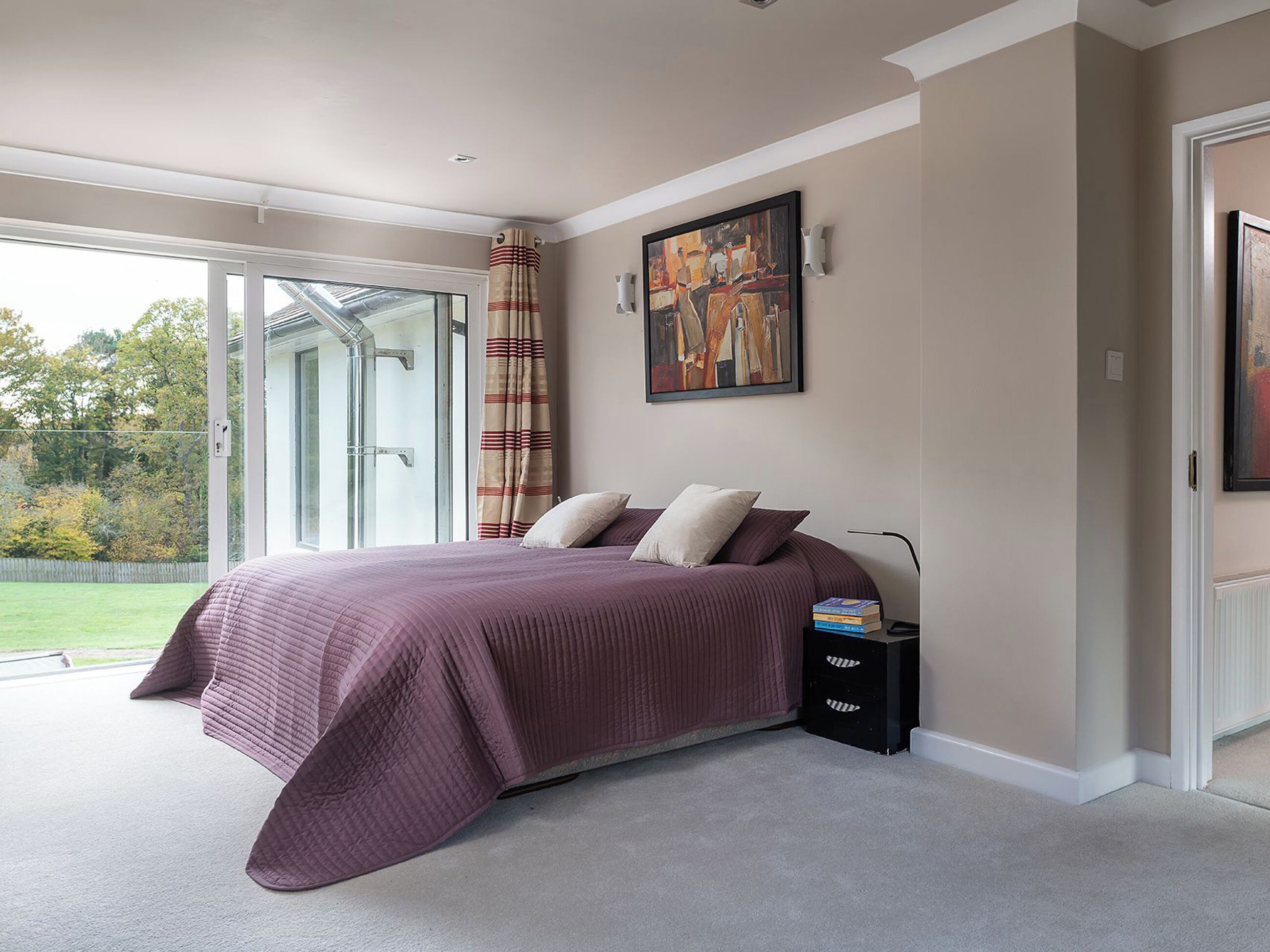 A bedroom with a large bed, a nightstand, a painting, and a sliding glass door to the outside.