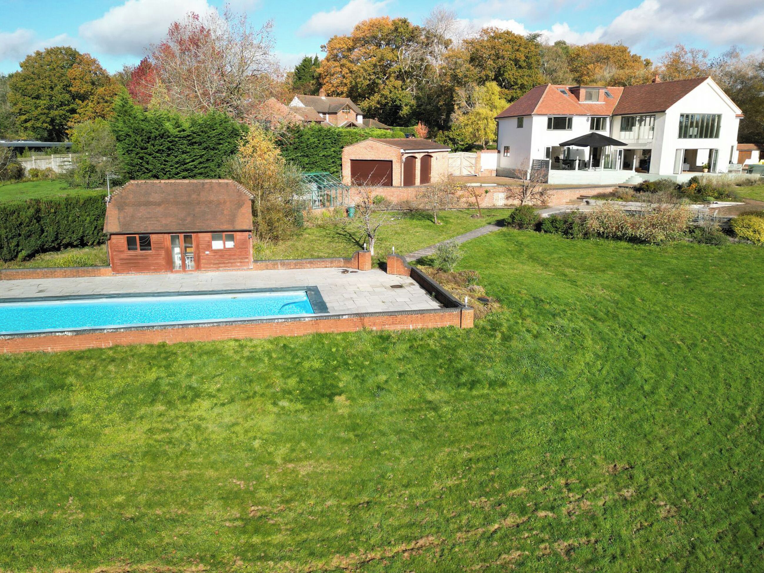 A residential property with a swimming pool, a detached garage, and a large house with a sloped roof.