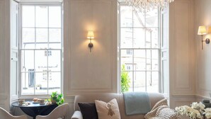 Una habitación con sofá, sillas, una mesa con pasteles y vistas a través de amplias ventanas.
