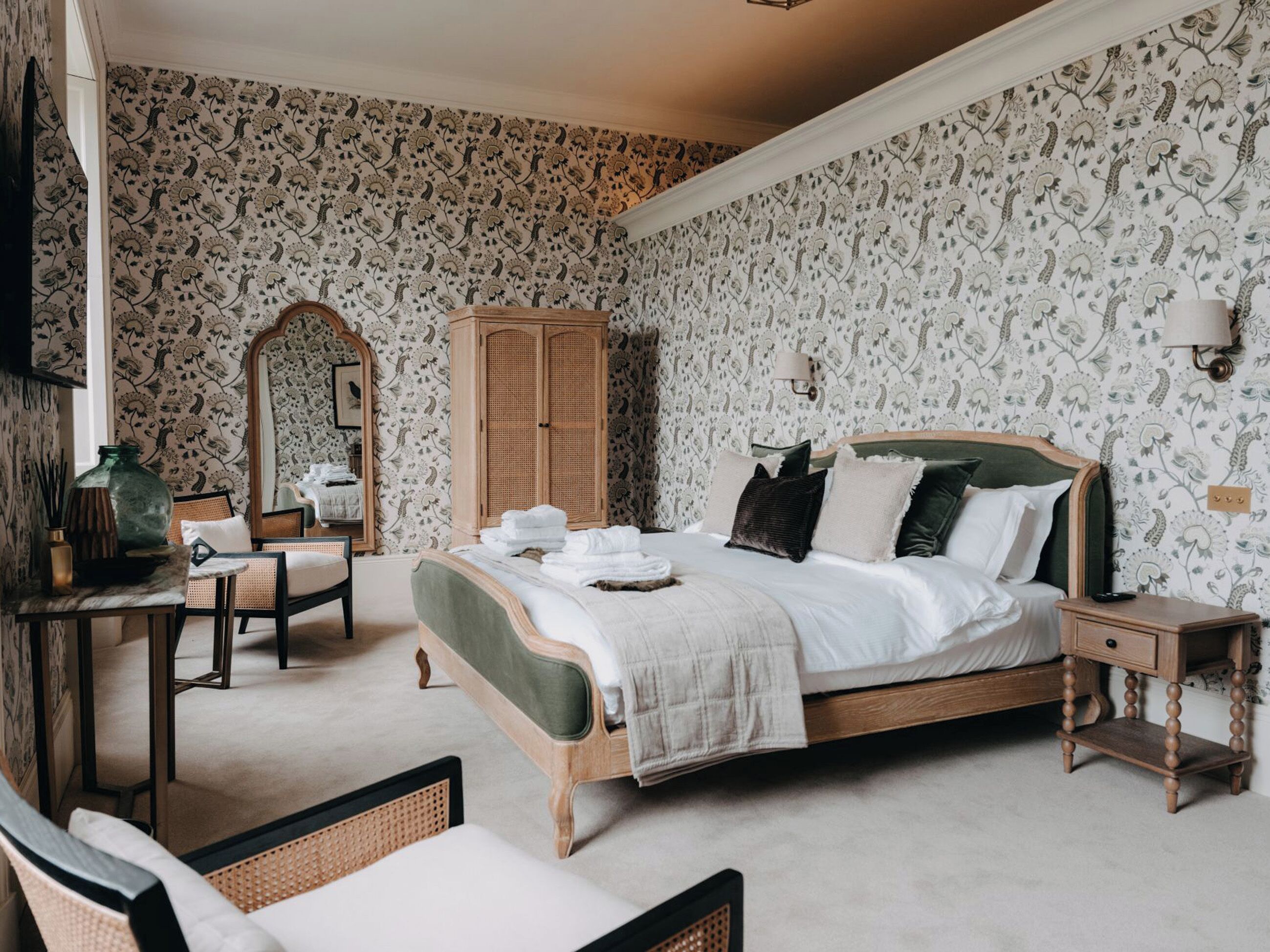 Une chambre à coucher avec un lit, une armoire en bois, un miroir, une chaise et une table de chevet.