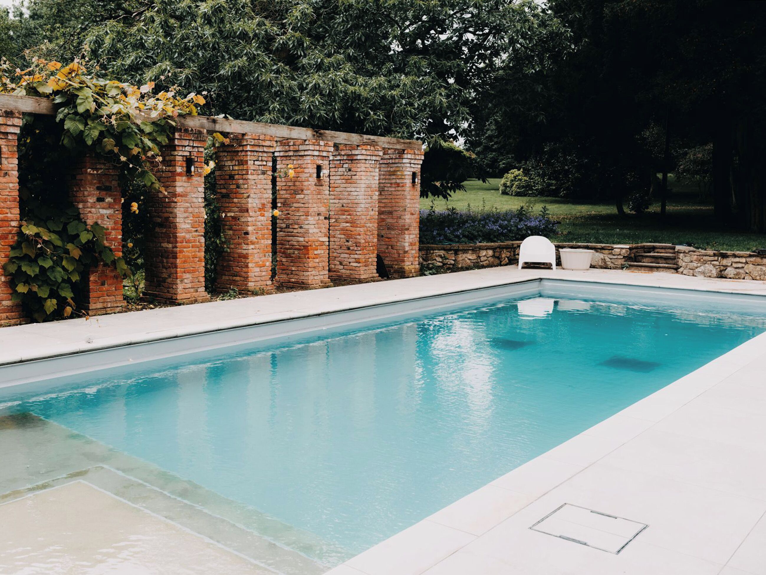 Une piscine rectangulaire à l’eau d’un bleu limpide, entourée d’un mur de briques et d’une terrasse carrelée de blanc.