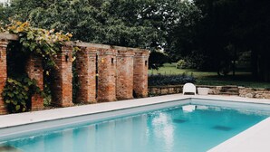 Una piscina rectangular con agua azul cristalina, rodeada por un muro de ladrillo y una terraza con baldosas blancas.