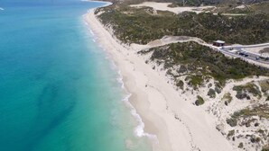 Un paysage côtier avec une plage de sable, une route qui serpente le long du rivage et une végétation clairsemée.