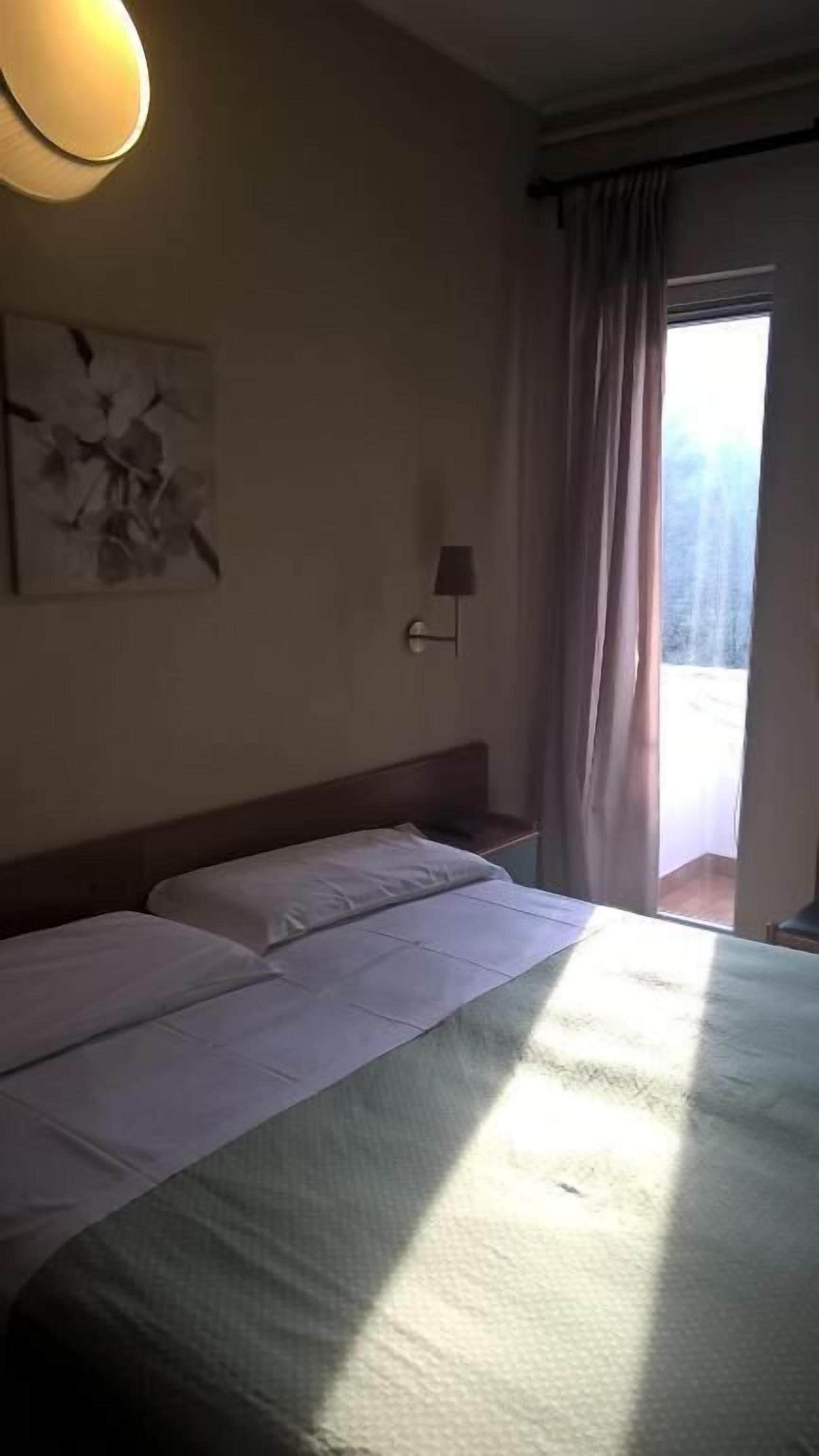 Ein Hotelzimmer mit einem Bett, einer Wandlampe und einem Fenster mit Vorhängen.