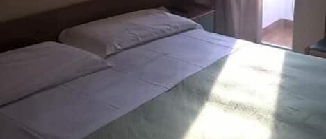 Une chambre d’hôtel avec un lit, une lampe fixée au mur et une fenêtre avec des rideaux.