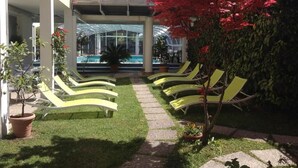 Uma área na piscina com espreguiçadeiras, uma piscina com paredes de vidro e uma galeria coberta.