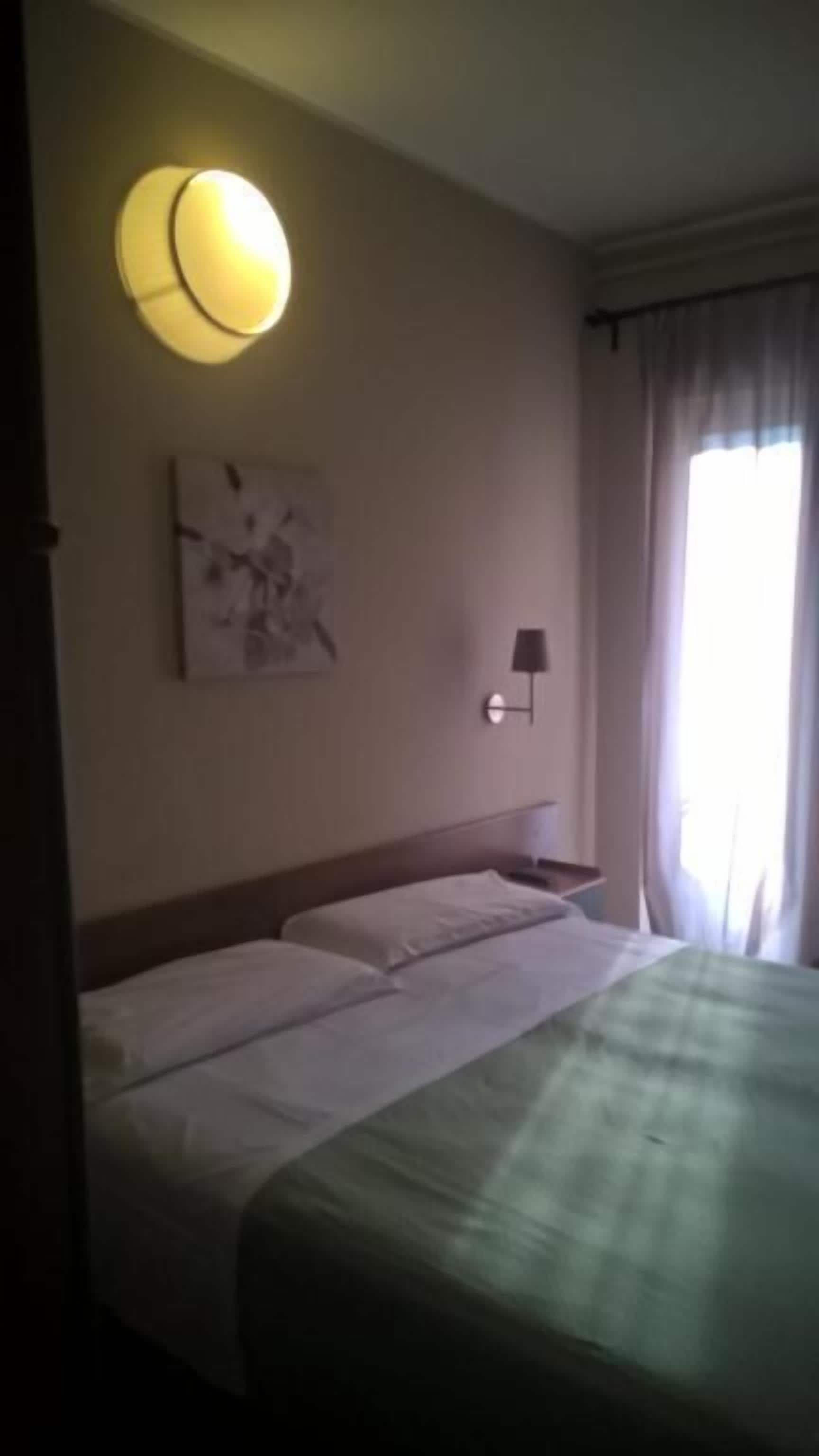 Una habitación de hotel con una cama, una lámpara de pared y un cuadro.