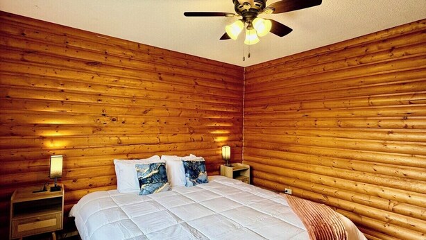 Ein Schlafzimmer mit Holzvertäfelung, einem Bett mit weißer Bettwäsche, einem Deckenventilator und Nachttischlampen.