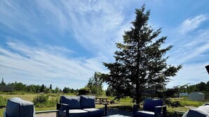 Ein Sitzbereich im Freien mit Tisch und Stühlen, einem Picknicktisch und einem großen Baum im Hintergrund.