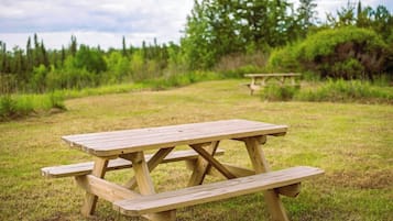 Une table de pique-nique en bois, installée dans un champ herbeux, avec des arbres en arrière-plan.