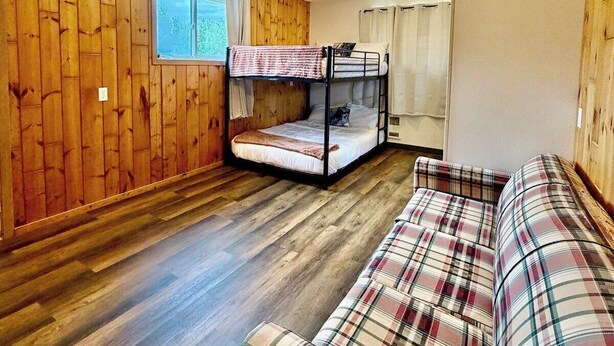 Una habitación con literas, un sofá escocés, paredes de madera y una ventana.