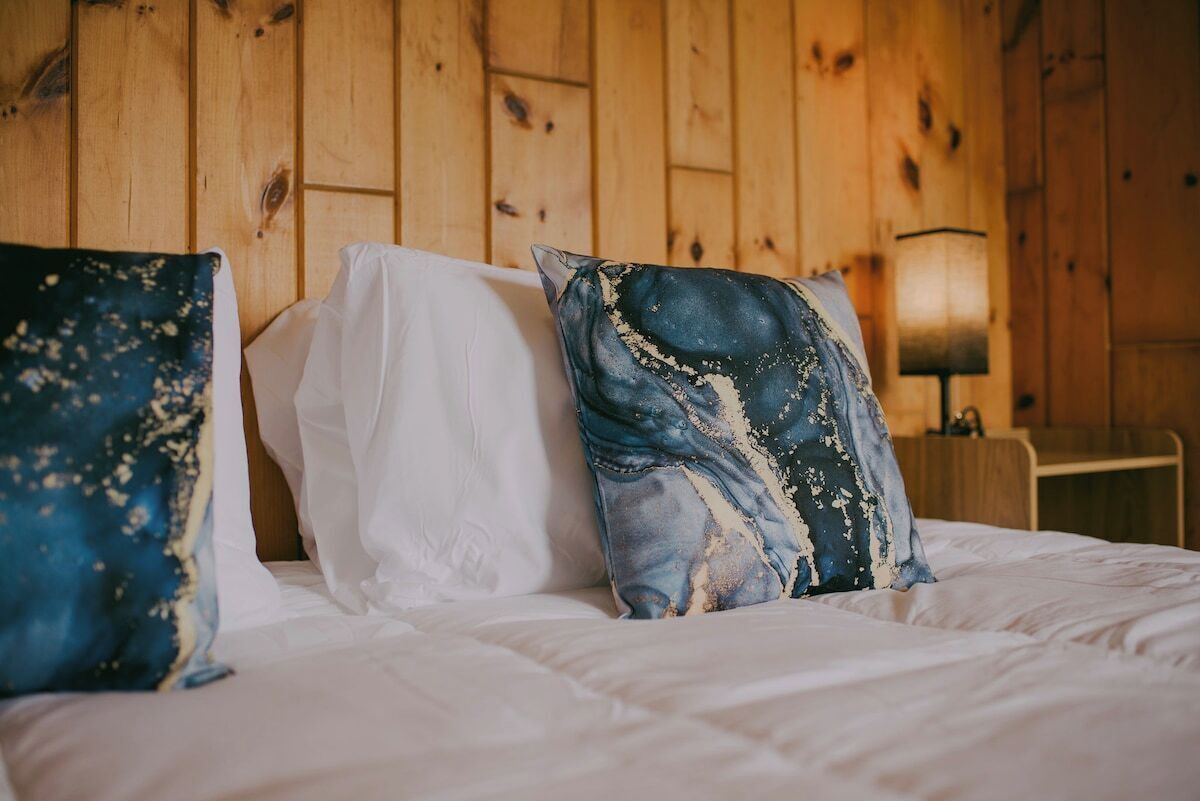 Una cama con ropa de cama blanca y dos almohadillas decorativas, una con estampado azul y blanco y la otra con un diseño abstracto azul y blanco.