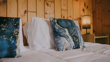 Un lit avec une literie blanche et deux coussins décoratifs, l’un avec un motif bleu et blanc et l’autre avec un motif abstrait bleu et blanc.