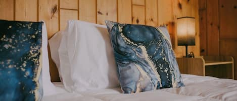 Una cama con ropa de cama blanca y dos almohadillas decorativas, una con estampado azul y blanco y la otra con un diseño abstracto azul y blanco.