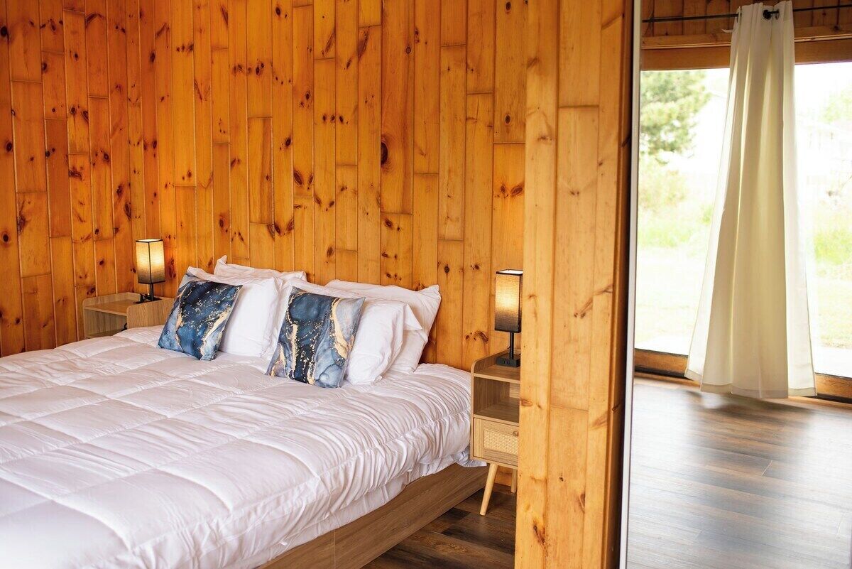 Un dormitorio con paneles de madera, una cama, almohadas, lámparas de noche y vistas por una ventana.