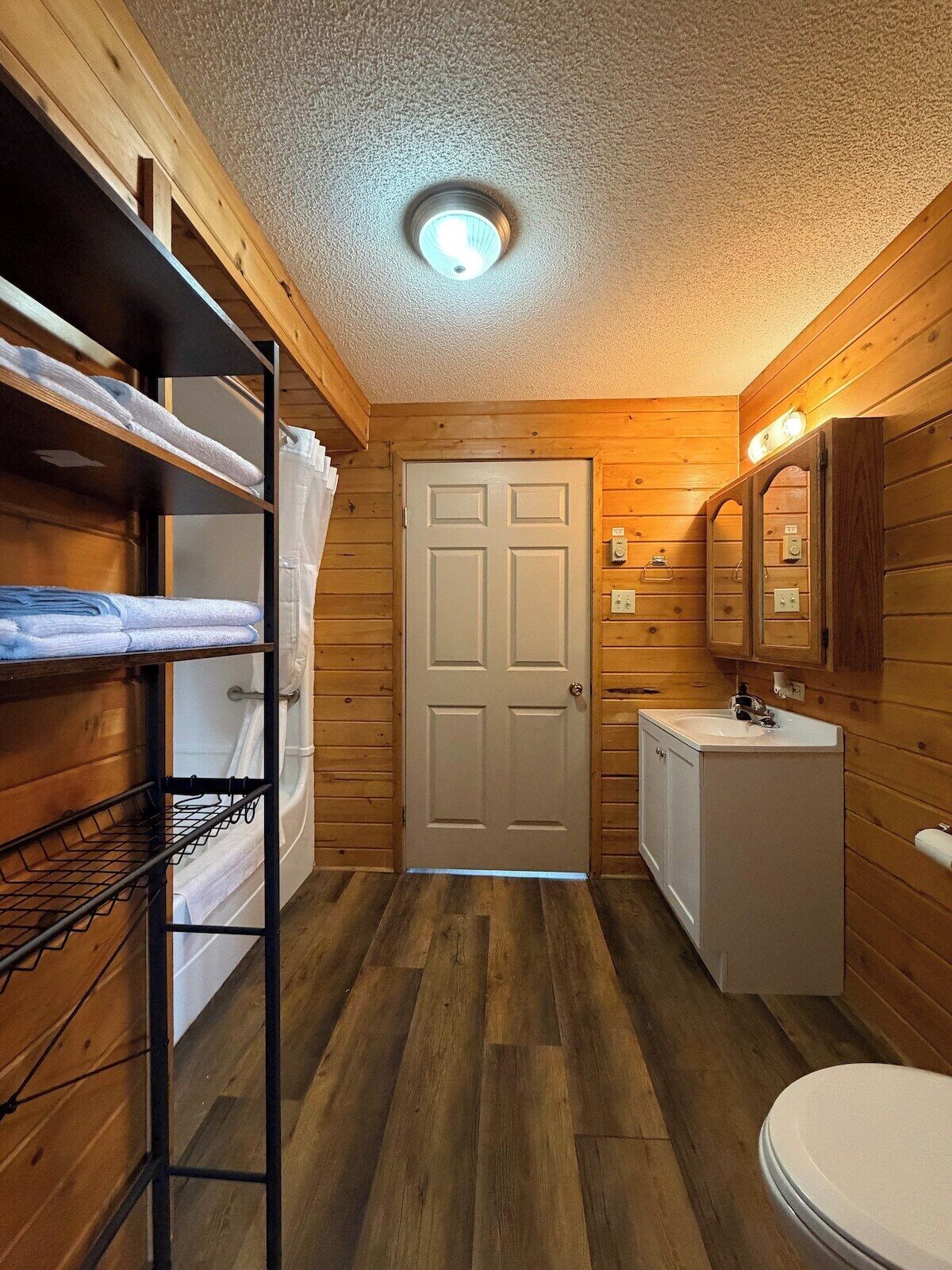 Une petite salle de bain aux murs en bois, avec une porte blanche, un lavabo et des toilettes.